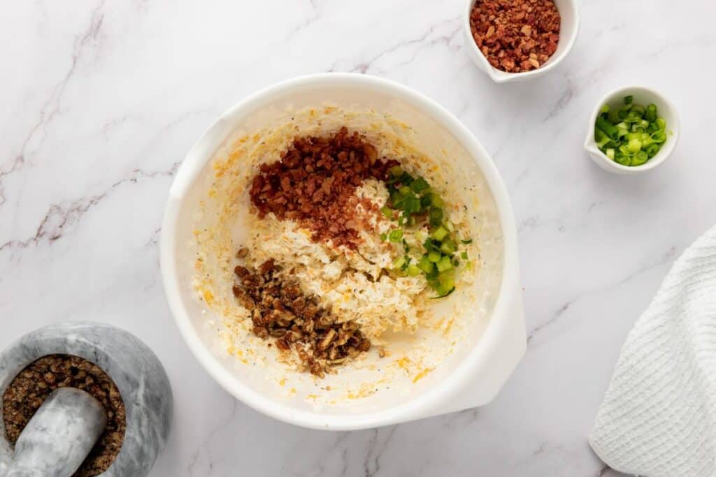 Stir in half the bacon bits, half the green onions, and half the chopped pecans.&nbsp;