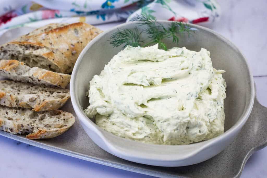 A bowl with a homemade Boursin Cheese with Fresh Herbs beside toasted baguette.