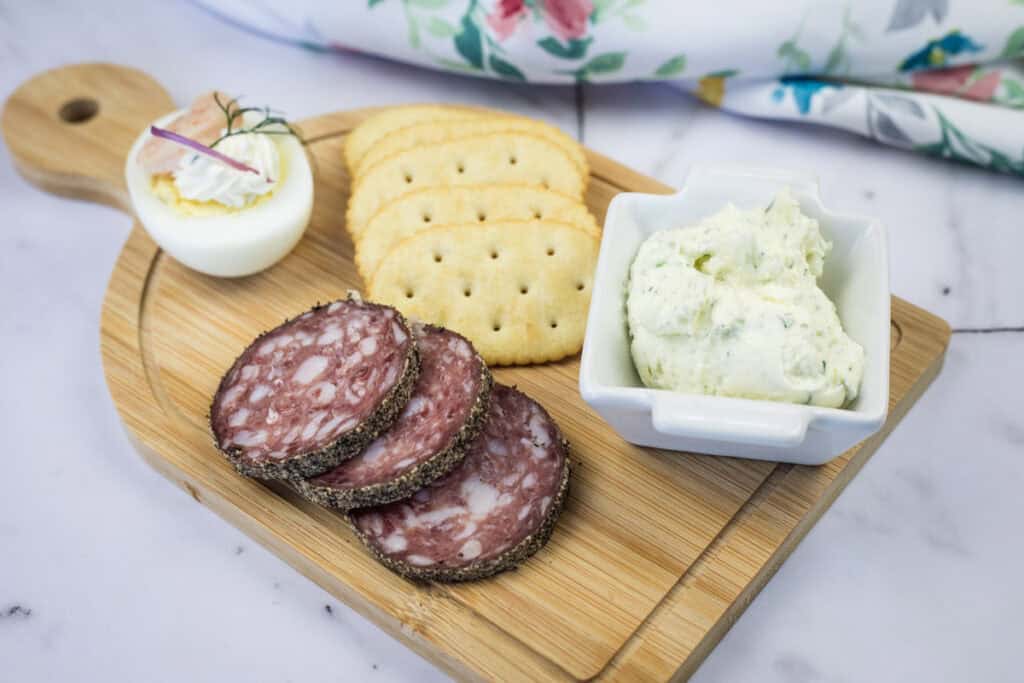 A board with Homemade Boursin Cheese with Fresh Herbs, crackers and a toasted baguette.