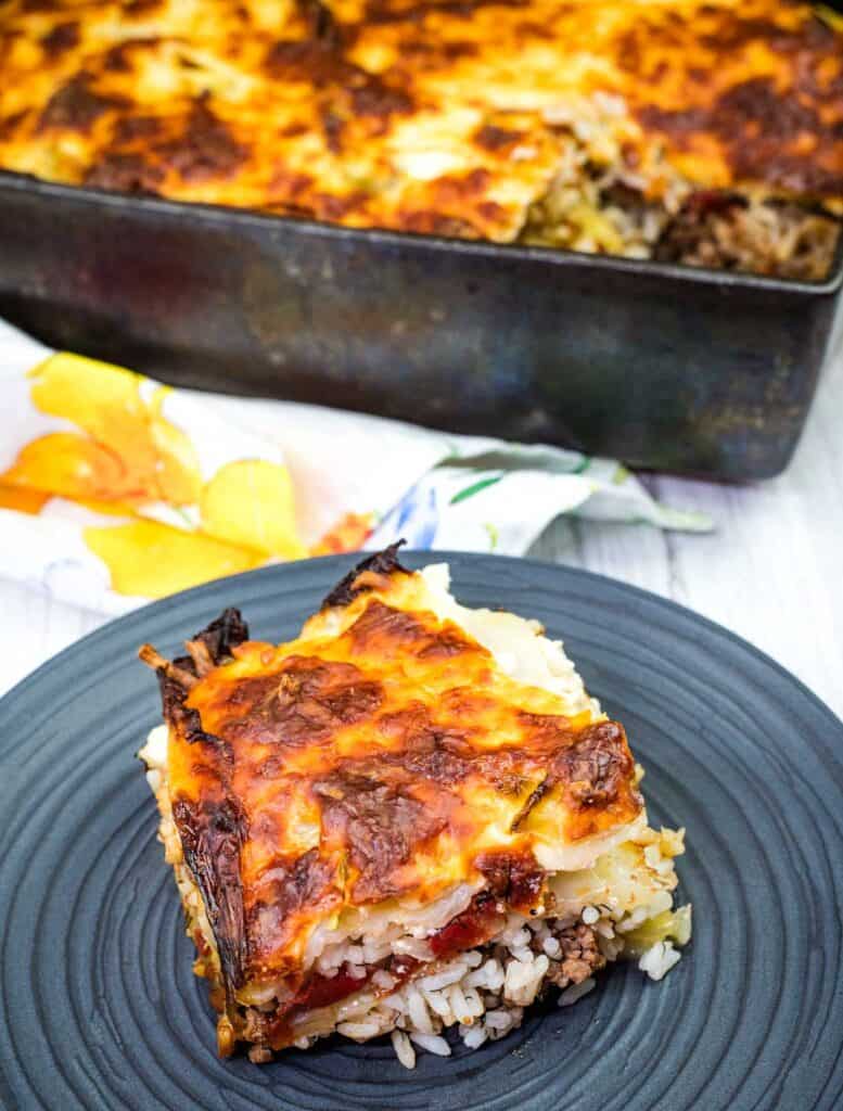 A black plate with a Cabbage Roll Casserole near a casserole dish.