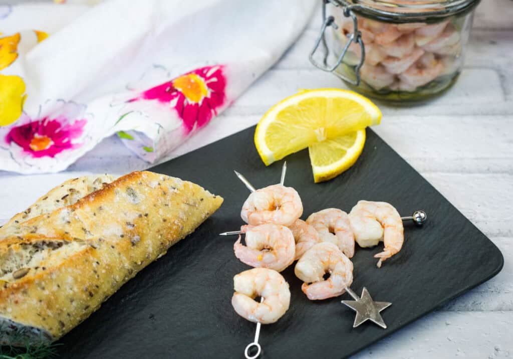 Pickled Shrimp on skewers with lemon slices on a black plate.