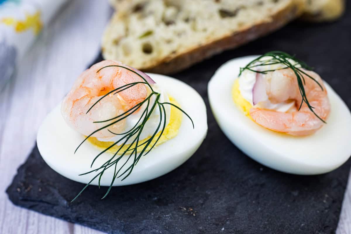 Two Pickled Shrimp Egg Shooter halves were placed on a slate board, next to slices of bread.