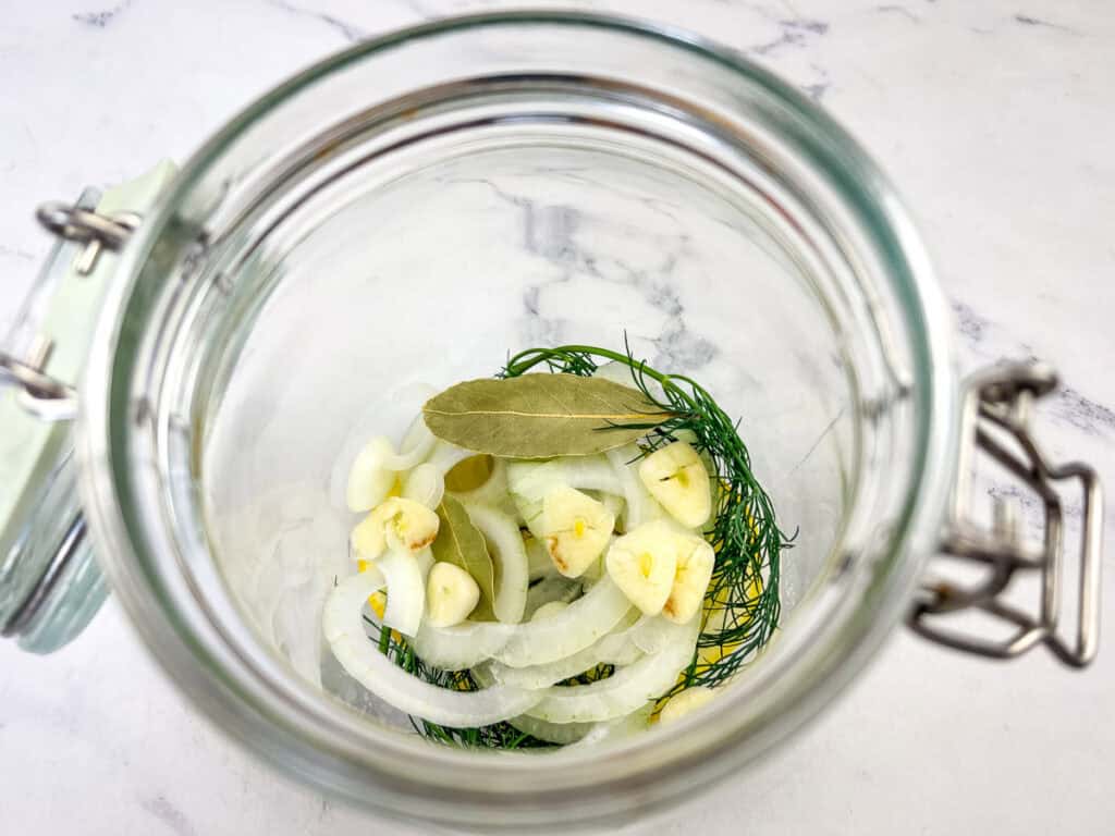 Place half the lemon, onion, and dill in the bottom of a glass jar.