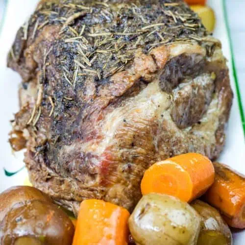 A long plate with a Slow Cooker Herb-Crusted Pork Roast with vegetables beside.