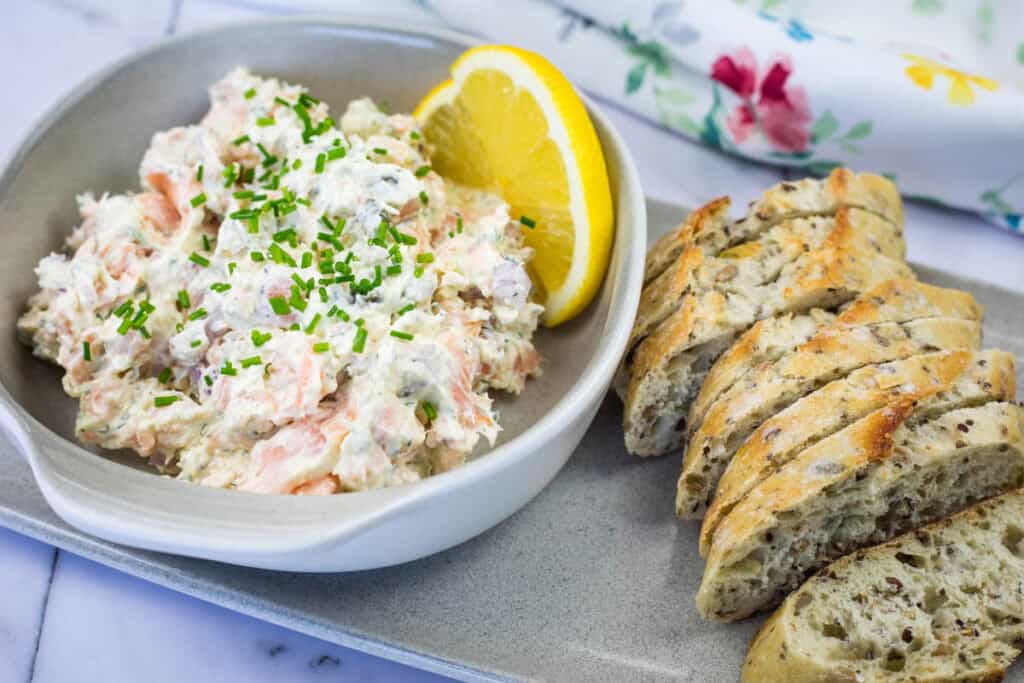 A bowl of Smoked Salmon Tartine with a lemon slice and toasted baguette.