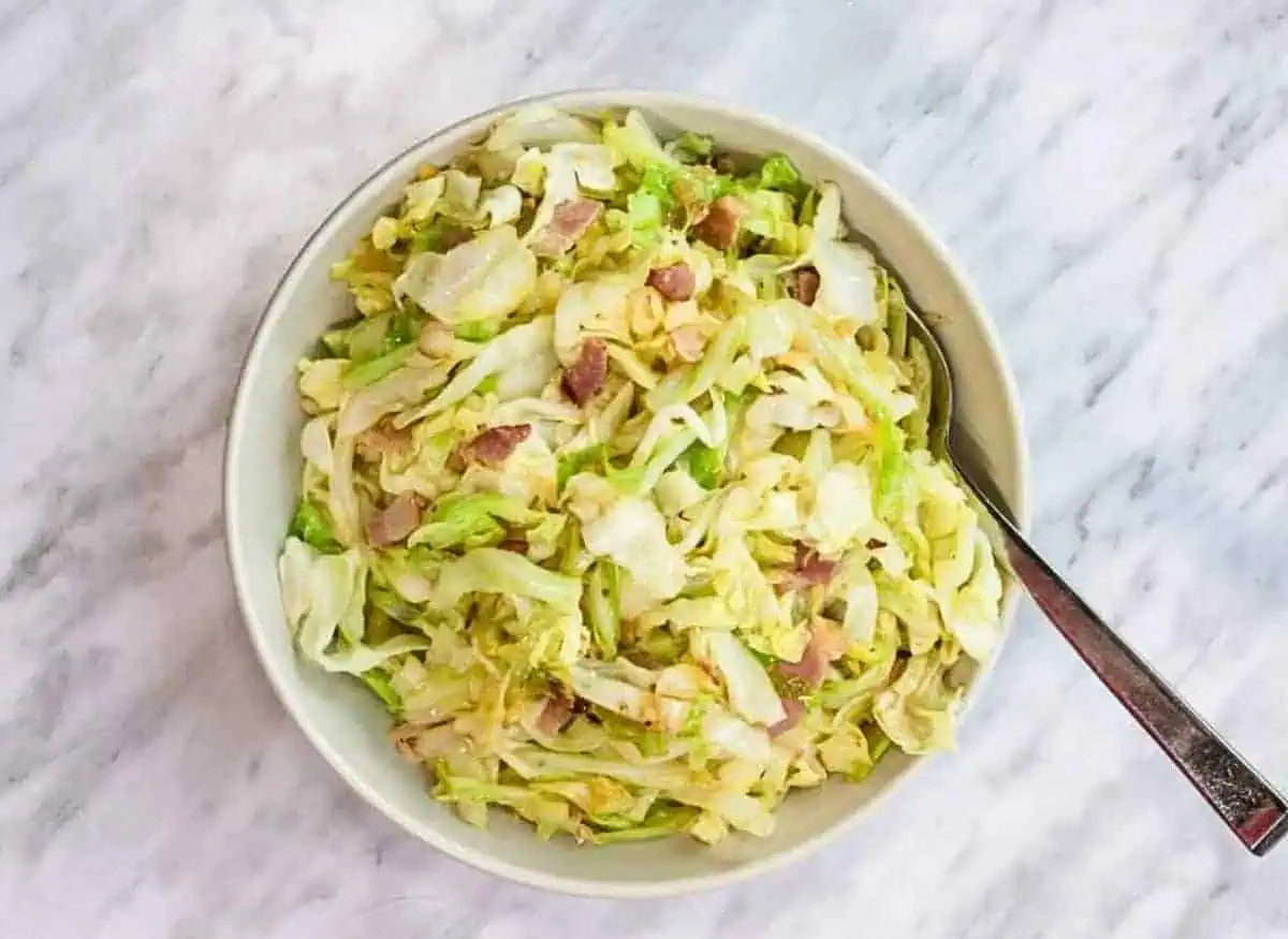 A bowl of cabbage salad with ham and bacon.