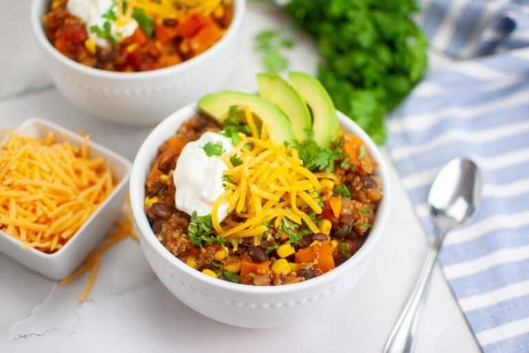 Two bowls of Sweet Potato Chili with Quinoa topped with grated cheese, cilantro, crema and avocado.
