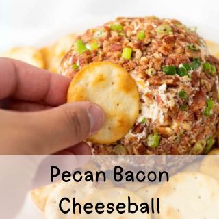 A hand holding a round cracker, reaching to dip into a pecan bacon cheeseball.