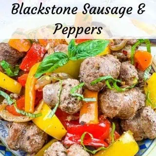 A dish of Blackstone sausage and peppers with red and yellow bell peppers, onions, and basil garnish.