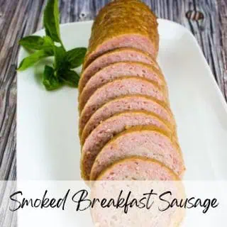 Sliced smoked breakfast sausage on a white plate, garnished with basil leaves. Text overlay reads "Smoked Breakfast Sausage.