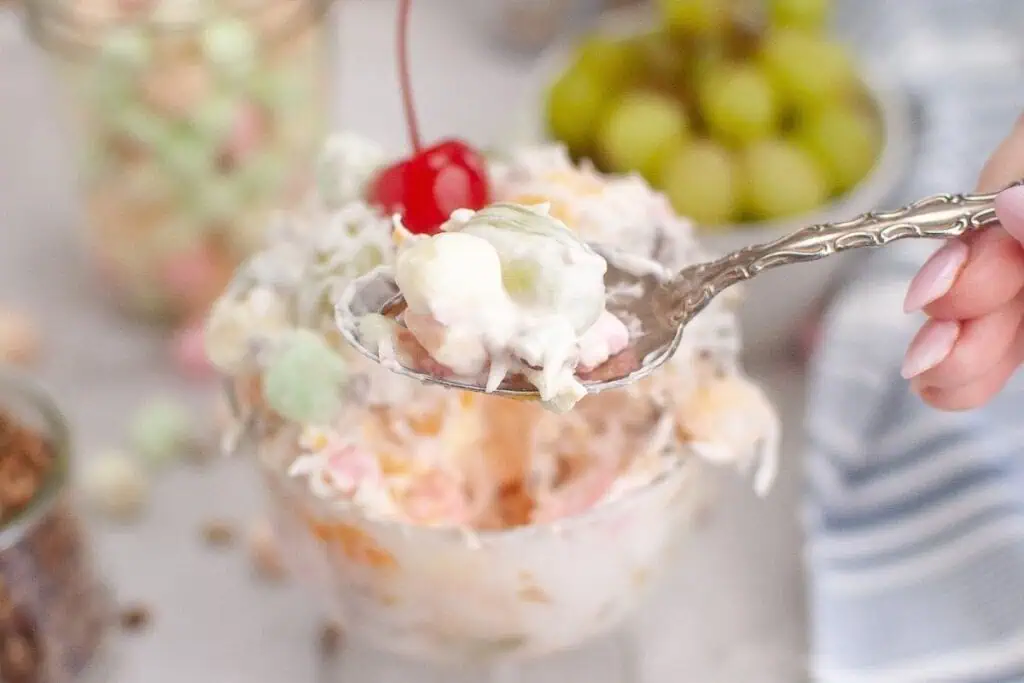A spoonful of Ambrosia salad is held above a bowl.