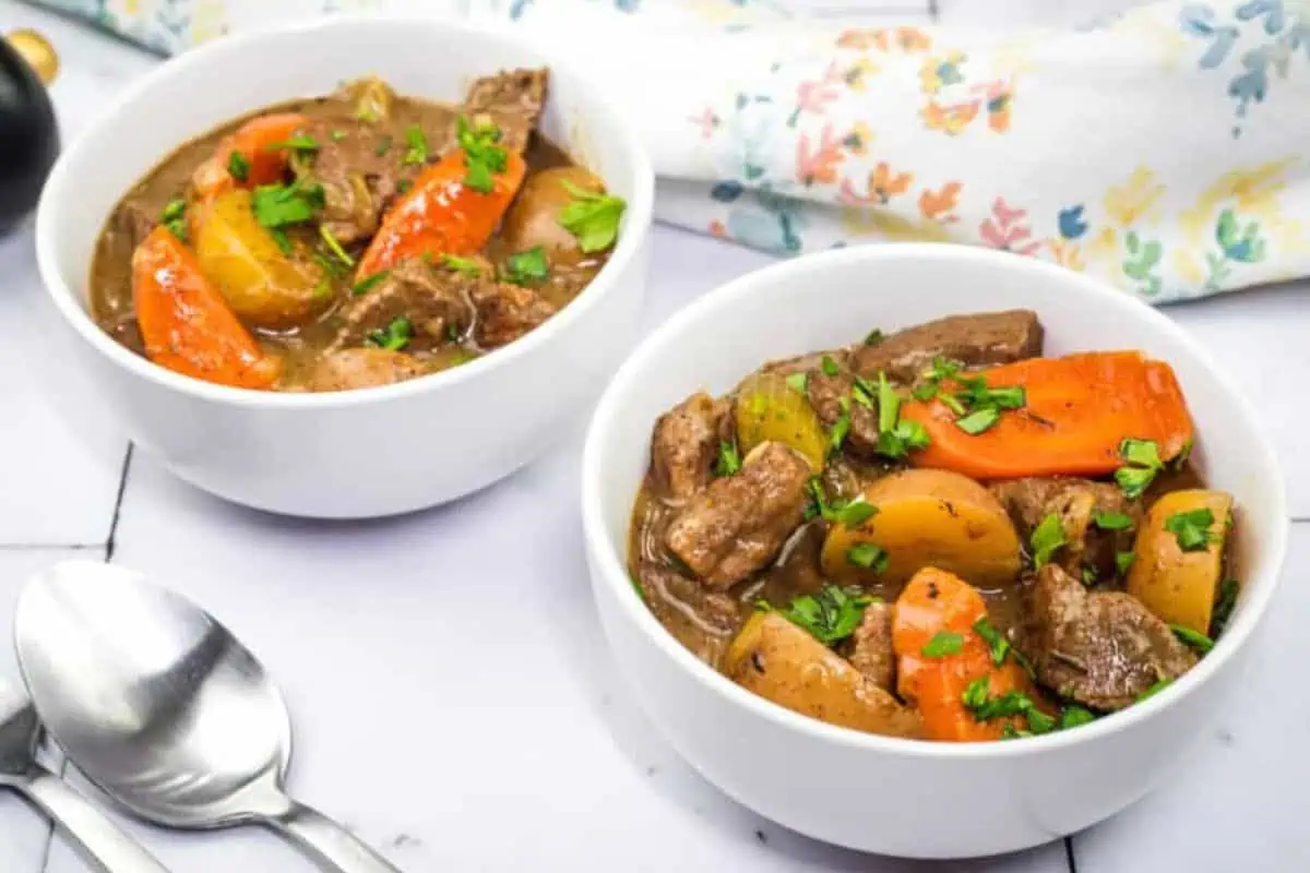 Two bowls of beef stew alongside two silver spoons.