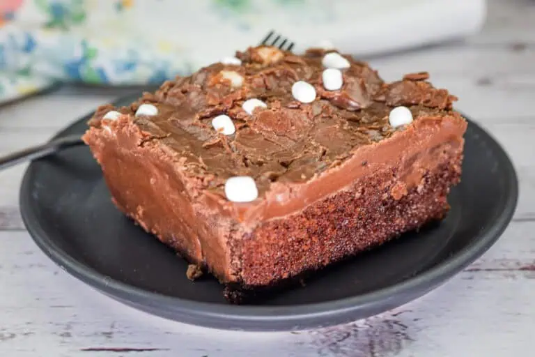 A slice of Grandma's Coca-Cola cake with chocolate frosting and small marshmallows on a black plate.