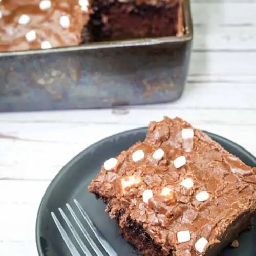 A square of Coca-Cola Cake on a black plate near the pan of cake.