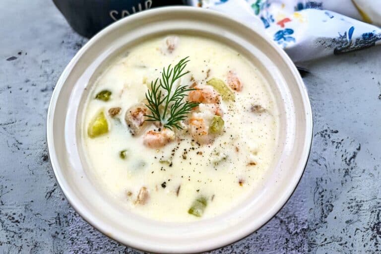 A bowl of fully loaded seafood chowder garnished with fresh dill and cracked pepper on top.