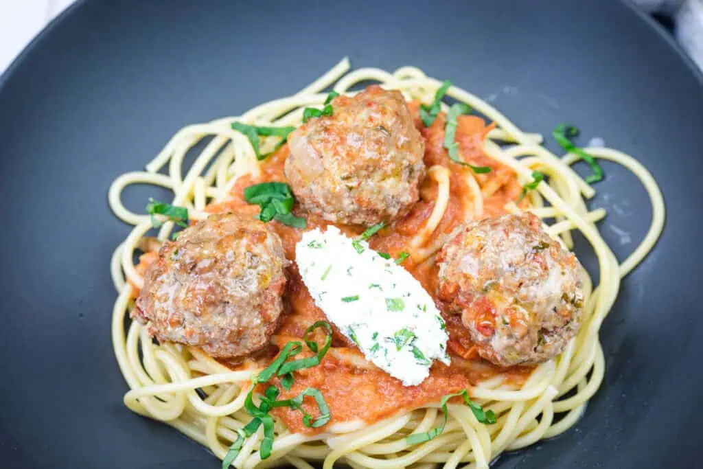 A delicious serving of spaghetti with ricotta meatballs and tomato sauce on a black plate.