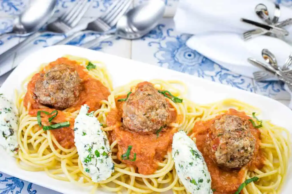 A white plate featuring spaghetti topped with ricotta meatballs and rich tomato sauce.