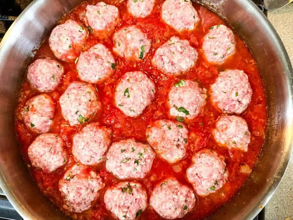 Meatballs nestled in simmering tomato sauce in a pan.