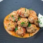 A serving of Ricotta Meatballs with Tomato Sauce on a black plate.