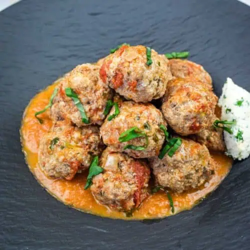 A serving of Ricotta Meatballs with Tomato Sauce on a black plate.