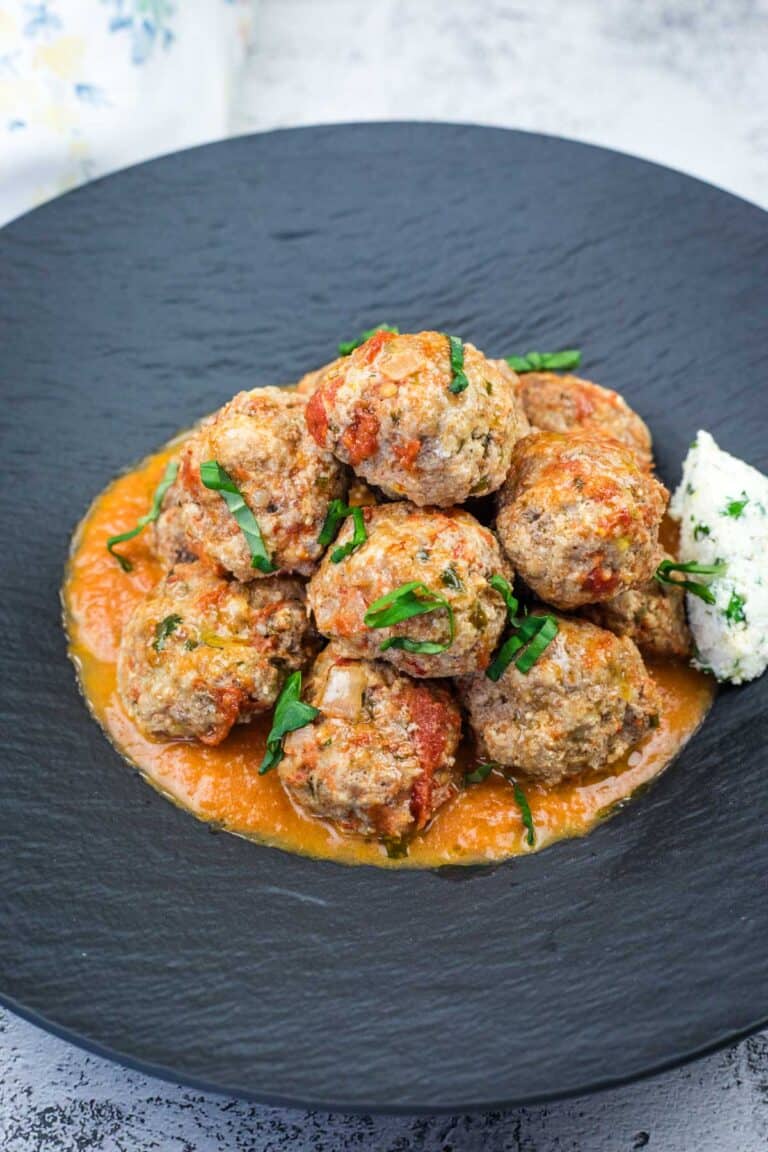 A serving of Ricotta Meatballs with Tomato Sauce on a black plate.