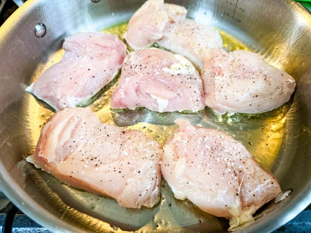 Raw chicken pieces seasoned with pepper and salt in a metal pan with olive oil.
