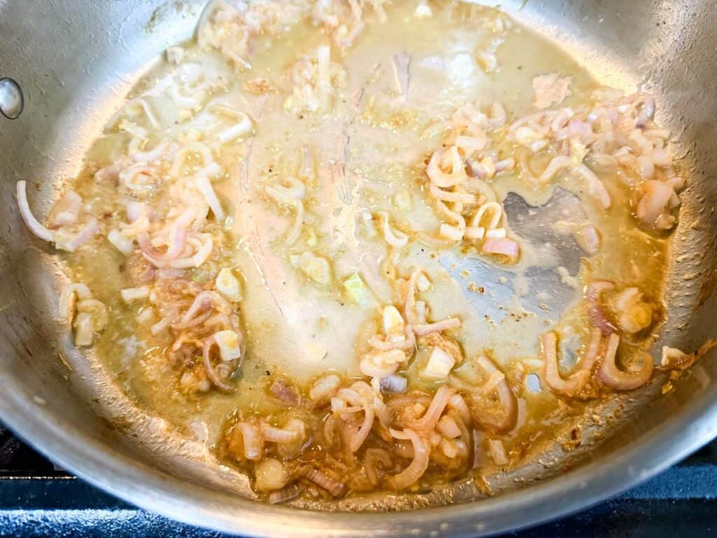 Sliced shallots and minced garlic saut&eacute;ing in a stainless steel pan with a light layer of oil.