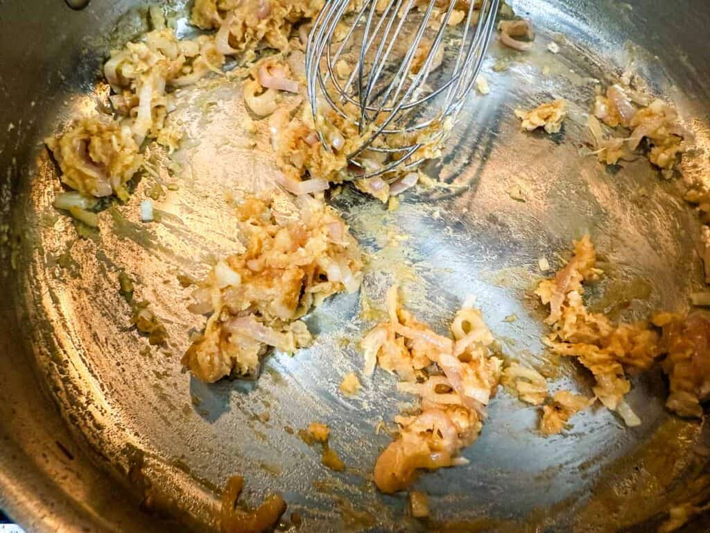 Onions and garlic saut&eacute;ing in a stainless steel pan with a whisk.