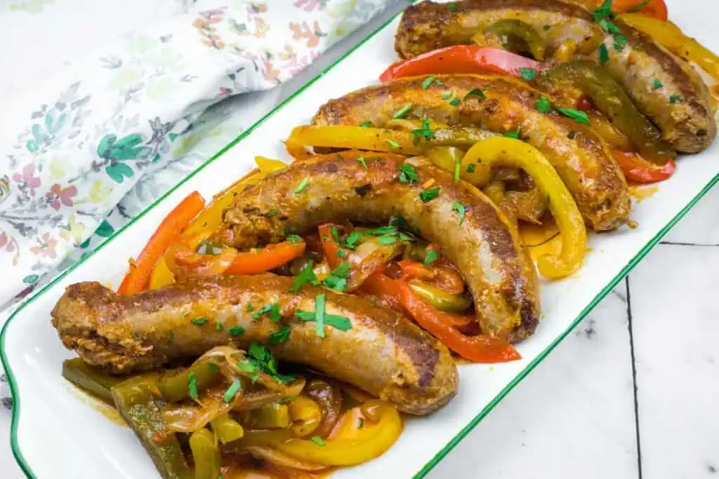 Plate of grilled sausages served with sautéed red, yellow, and green bell peppers, garnished with chopped herbs.