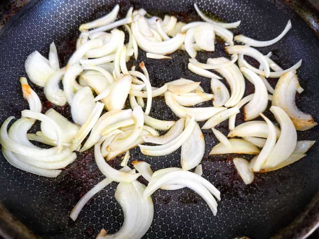Sliced onions cooking in a frying pan, partially caramelized.