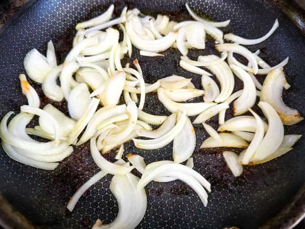 Sliced onions cooking in a frying pan, partially caramelized.