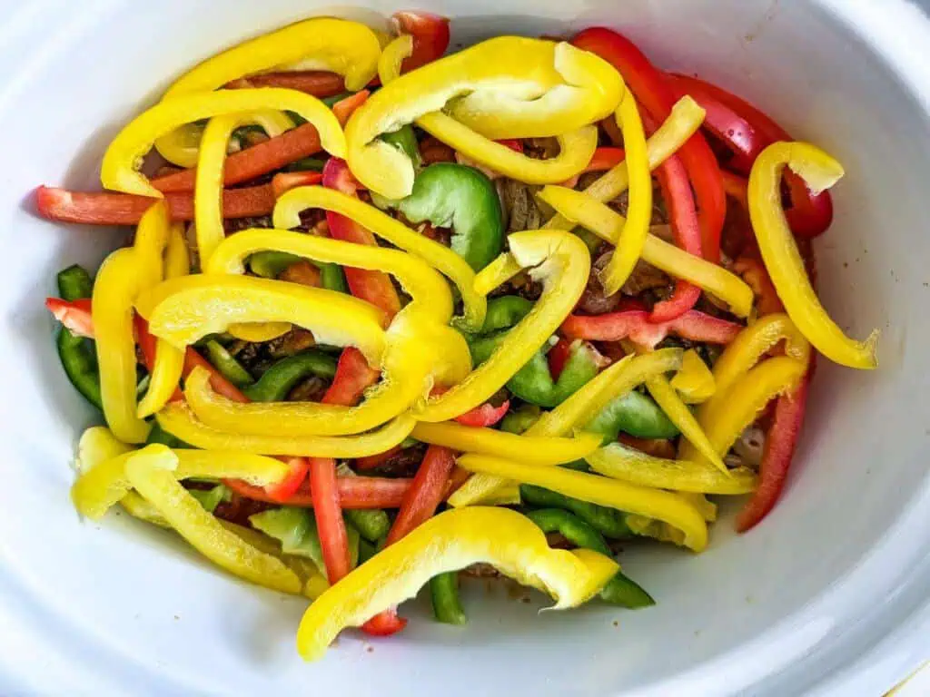 Sliced red, yellow, and green bell peppers in a white bowl.