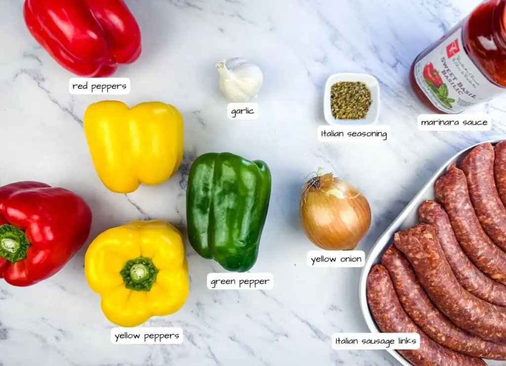 Ingredients arranged on a marble surface: red and yellow bell peppers, green pepper, garlic, yellow onion, Italian sausage links, Italian seasoning, and marinara sauce.