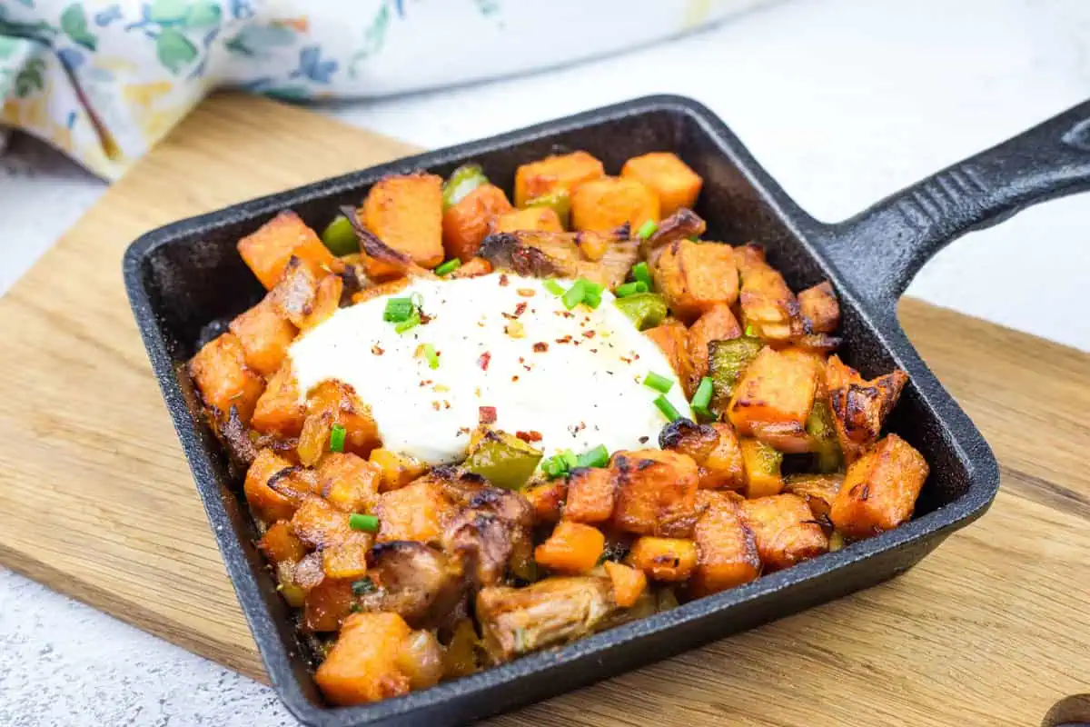 Cast iron skillet with sweet potato hash with pulled pork and garnished with chopped chives.