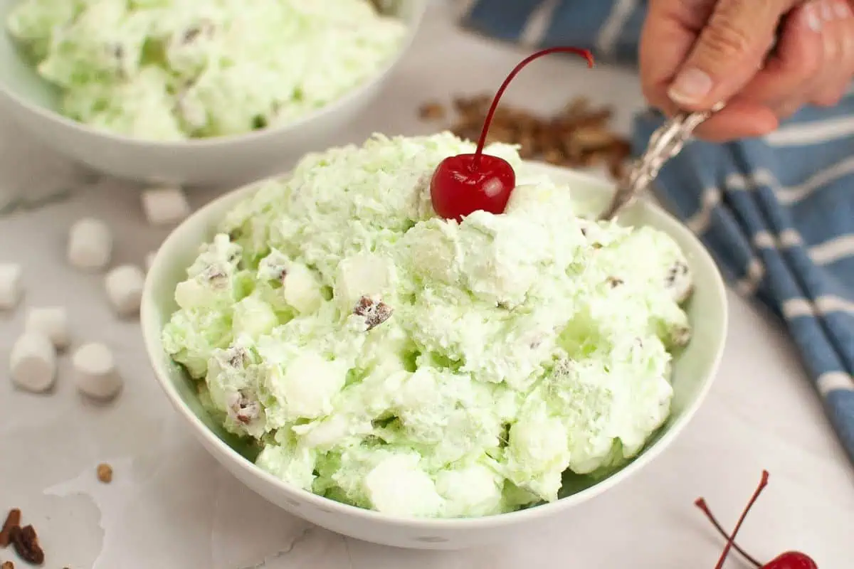 A bowl of Watergate salad topped with a cherry.