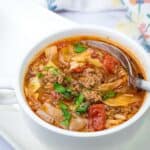 A spoon getting small amount of Cabbage roll soup in a white bowl.
