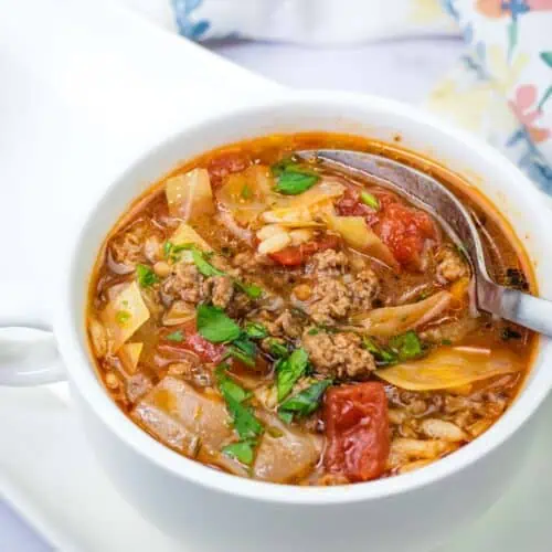 A spoon getting small amount of Cabbage roll soup in a white bowl.