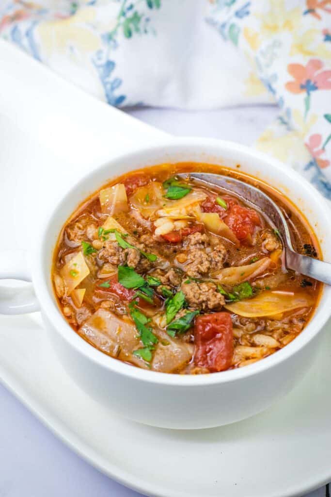A spoon getting small amount of Cabbage roll soup in a white bowl.