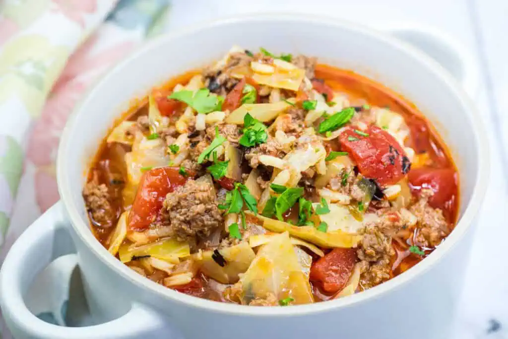 A bowl of cabbage roll soup with ground meat, chopped tomatoes, and rice, garnished with fresh parsley.