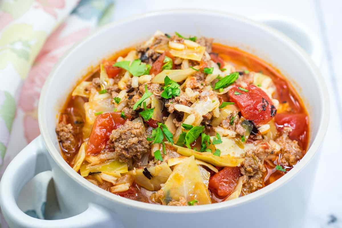 A bowl of cabbage roll soup with ground meat, chopped tomatoes, and rice, garnished with fresh parsley.