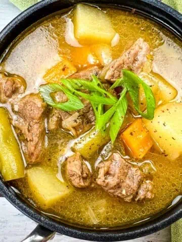 A pot of Steak and Potato Soup garnished with sliced green onions.