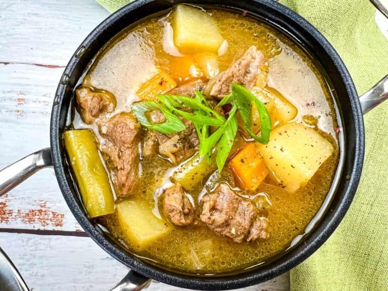 A pot of Steak and Potato Soup garnished with sliced green onions.