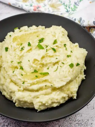 Mashed potatoes with cream cheese topped with melted butter and garnished with fresh parsley.