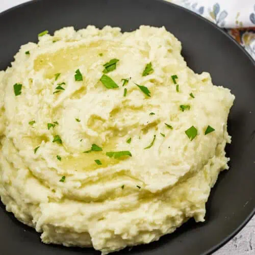 Mashed potatoes with cream cheese topped with melted butter and garnished with fresh parsley.