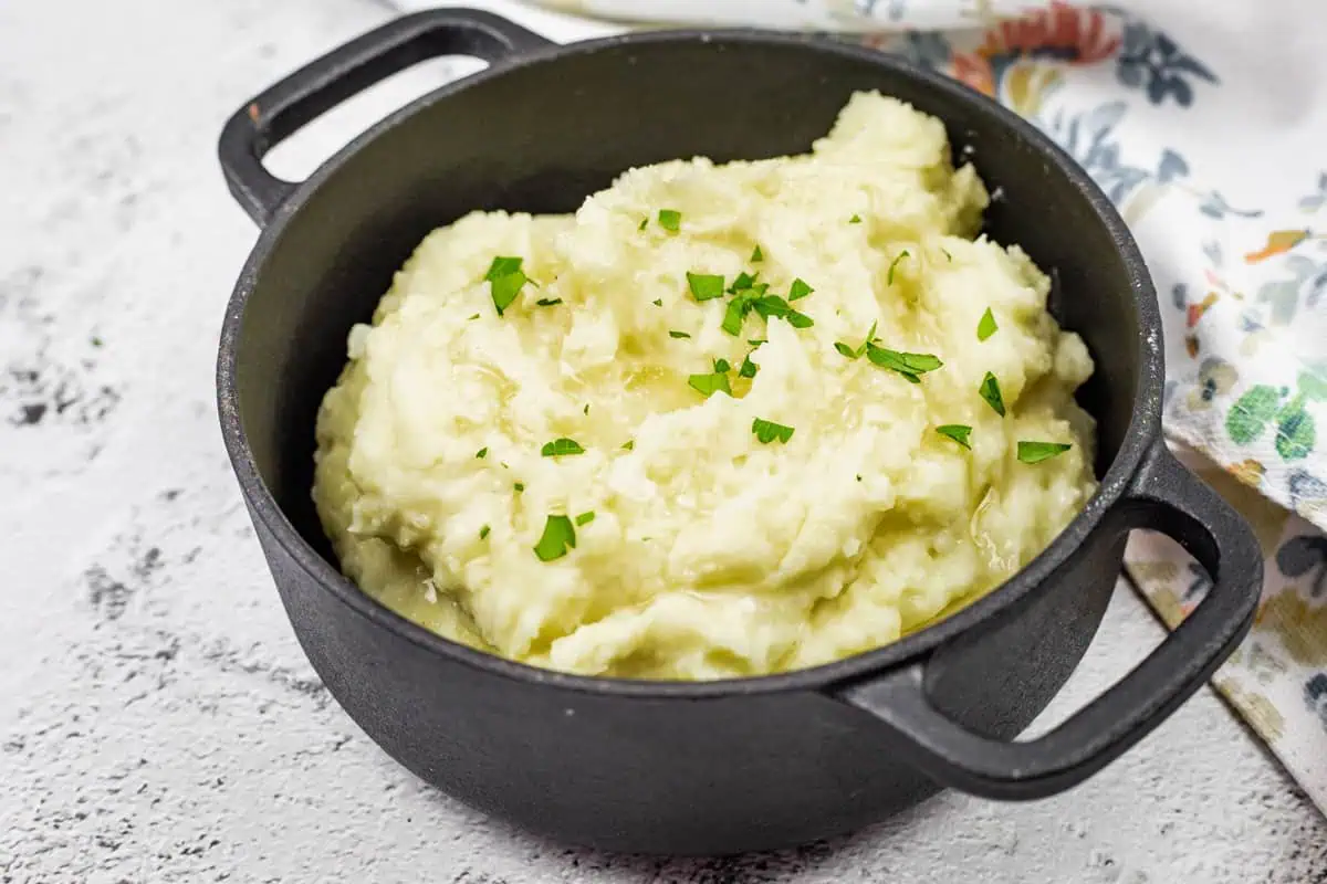 A black pot filled with Creamiest mashed potatoes, topped with chopped parsley.