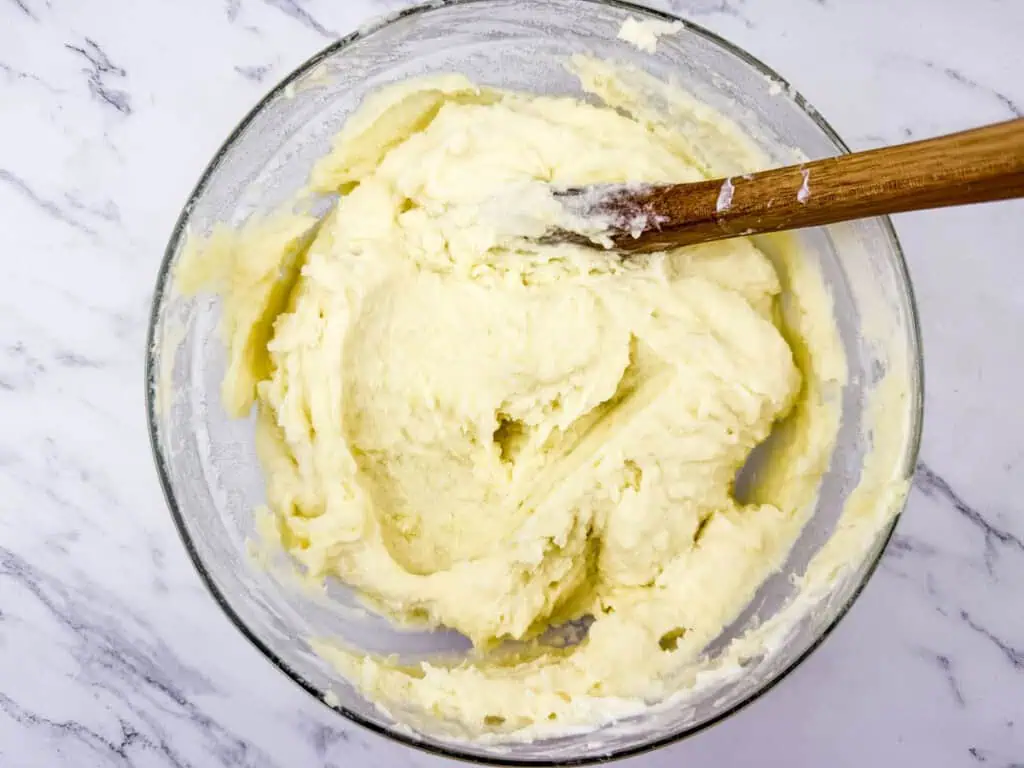 A glass bowl filled with creamy, smooth mashed potatoes being mixed with a wooden spoon.