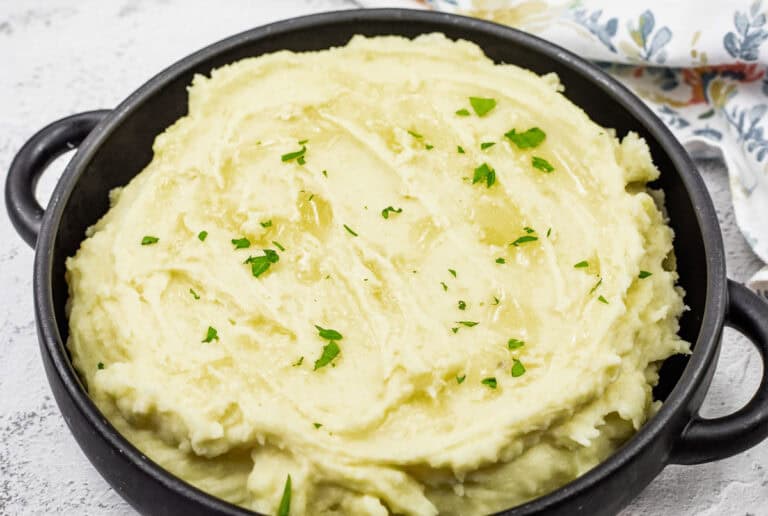 Mashed potatoes with cream cheese topped with melted butter and garnished with fresh parsley.