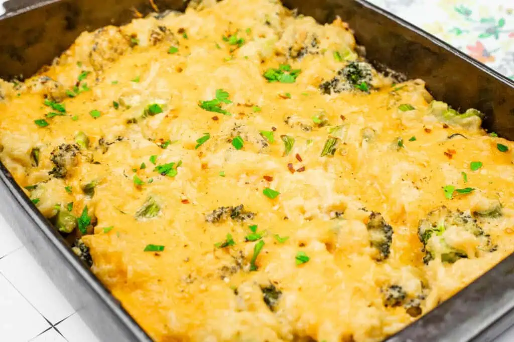 Broccoli Rice Casserole with Fresh Broccoli in a black baking dish, topped with golden melted cheese, fresh parsley, and red pepper flakes for garnish.