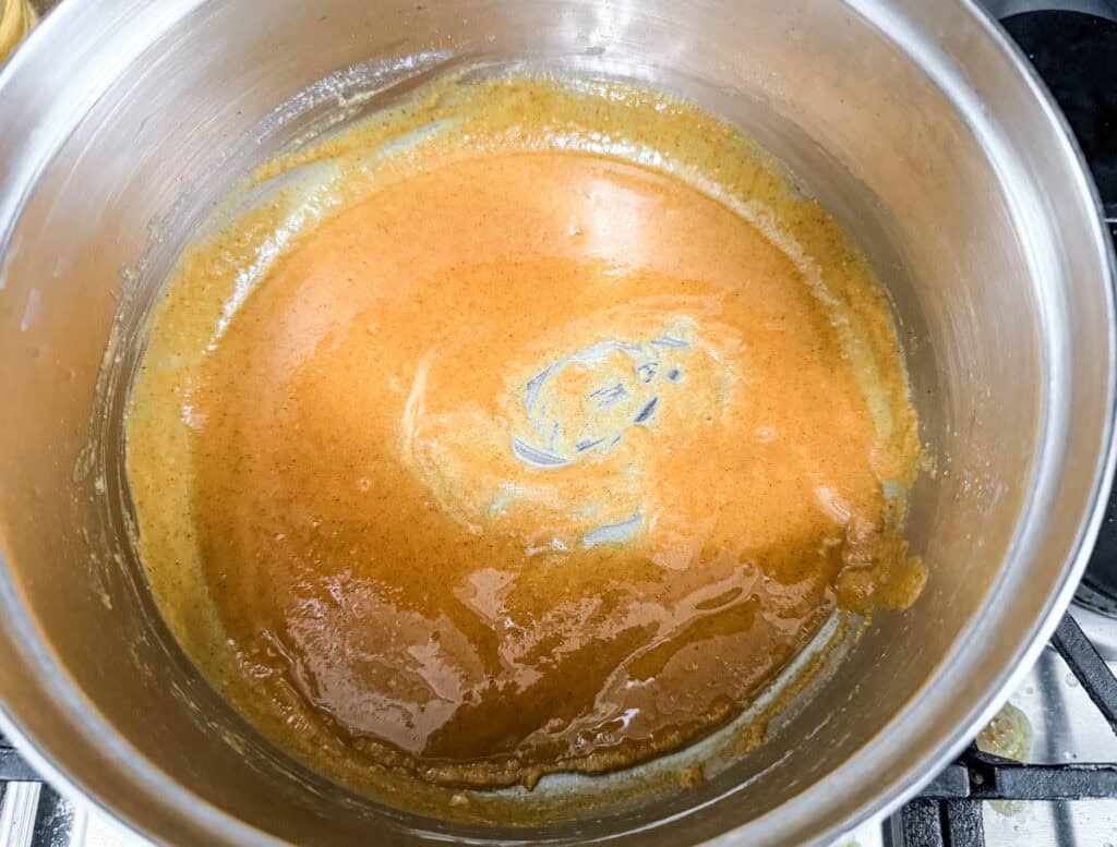 Roux mixture being cooked in a stainless steel pot, showing a smooth, golden-brown texture as the base for a creamy sauce.