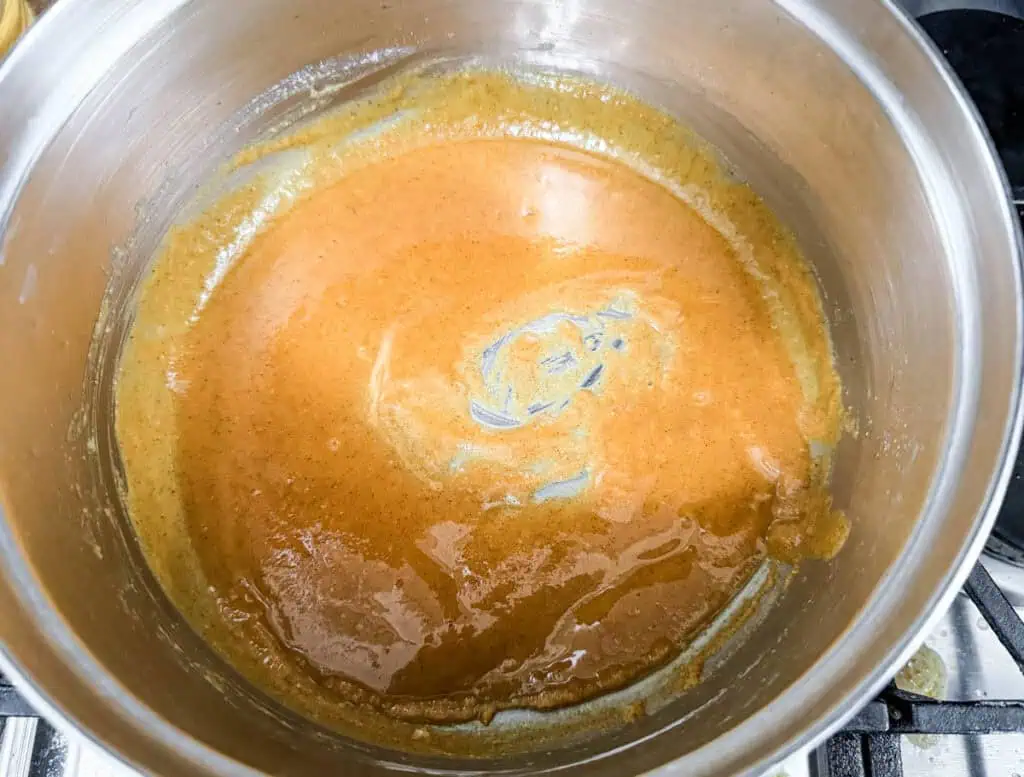 Roux mixture being cooked in a stainless steel pot, showing a smooth, golden-brown texture as the base for a creamy sauce.